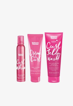 Drie haarverzorgingsproducten: een roze mousse spuitbus, een roze krulcontrolcrème tube en een roze shampoo fles, allemaal van het merk Umberto Giannini.