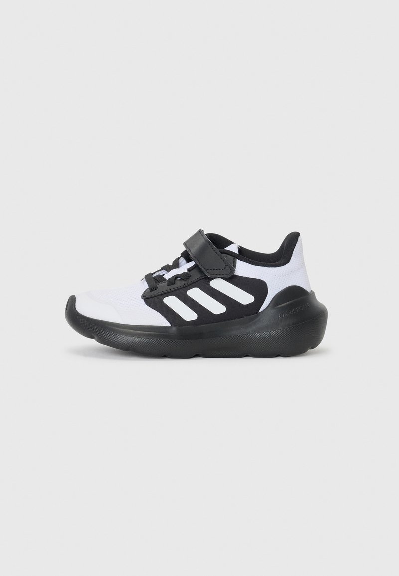Chaussure de sport blanche et noire avec un dessus en mesh, dotée d'une sangle noire, de trois rayures blanches et d'une épaisse semelle en caoutchouc noir.