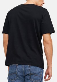 Schwarzes Baumwoll-T-Shirt mit kurzen Ärmeln, Rundhalsausschnitt, lockerer Passform, glatter Textur und Saum, der auf der Taille endet, getragen mit blauen Jeans.