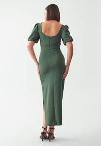 Zelena dolga obleka s prilagojenim rezom, nabranimi rokavi in odprtim hrbtom. Ima stranski razporek in zadrgo na hrbtu. Gladka tekstura.