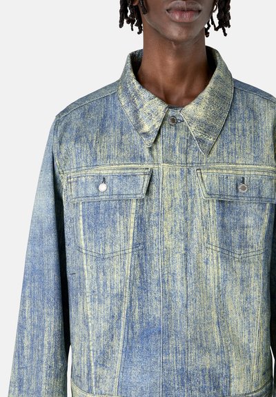Chaqueta de denim con un patrón desgastado en azul y amarillo. Presenta un cuello clásico, dos bolsillos en el pecho y cierre frontal con botones.
