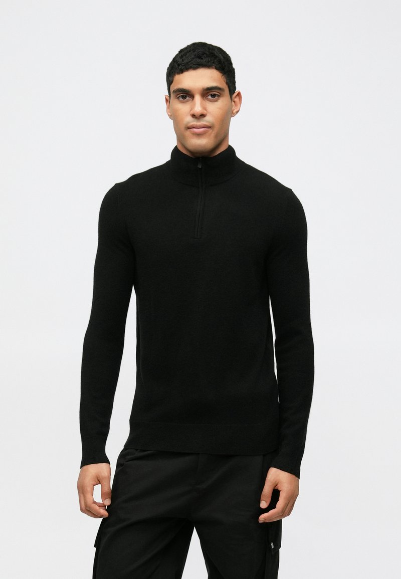 Juodas megztinis su aukštu kaklu, ilgomis rankovėmis, pagamintas iš minkštos, tekstūrinės medžiagos. Turi pusiau užtrauktuką ant apykaklės, prilipnanti siluetas.