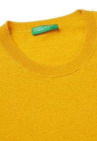 Żółty dzianinowy sweter z okrągłym dekoltem i ribbami. Ozdobiony metką z logo "United Colors of Benetton" w kolorze zielonym. Gładka struktura.