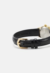 Bracelet de montre en cuir noir avec une finition texturée, doté d'une boucle en métal doré et d'un cadran de montre rond argenté.