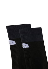 Calcetines negros con una textura acanalada y una banda gris oscura en la parte superior. Presentan un patrón de logo estilizado en blanco en el costado.
