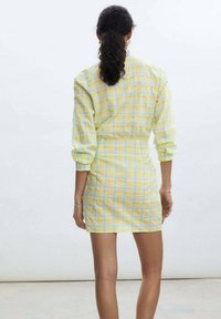 Žluté a modré kostkované šaty s dlouhými rukávy, úzkým pasem a délkou nad kolena, vyrobené z lehké strukturované tkaniny.