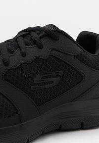 Scarpa da ginnastica nera con tomaia in pelle testurizzata, pannelli in rete e suola in gomma, che presenta un design elegante e accenti cuciti.