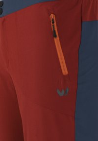 Punaiset ja laivastonsiniset ulkoiluhousut, joissa on sivutasku oranssilla vetoketjulla. Materiaali on teksturoitua; alareunassa on logo.