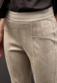 Béžové semišové kalhoty s pohodlným strukturálním pasem, zdobené dvěma bočními kapsami a přiléhavým střihem, který zvýrazňuje čisté švy.