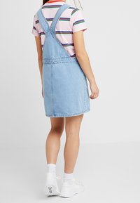 Ljusblå denim overallklänning, midja-thigh längd, med justerbara remmar, kombinerad med en randig t-shirt med kort ärm och vita sneakers.