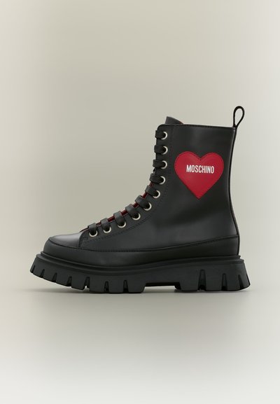 Botte de combat en cuir noir avec semelle épaisse, patch cœur rouge et texte blanc "Moschino" sur le côté, vue de l'extérieur.