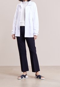 Vit kavaj över en krämfärgad polotröja, kombinerat med marinblå vida byxor och marinblå sandaler med vita sulor.