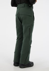 Groene waterdichte sneeuwpants met verstelbare bandjes, ritszakken en een taps toelopend ontwerp. Verstevigde manchetten en ritsen onderaan.