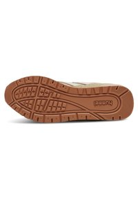 Basket Hummel avec semelle en caoutchouc offrant une adhérence texturée, tige beige avec accents texturés et détails de marque sur la semelle.