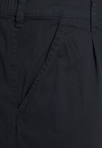 Calças pretas em algodão com uma textura suave, apresentando uma frente lisa e bolsos laterais, com costuras detalhadas ao longo das costuras.