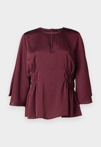 Blusa borgogna con scollatura rotonda, maniche a campana lunghe e dettagli arricciati ai lati. Realizzata in tessuto morbido con una vestibilità rilassata.