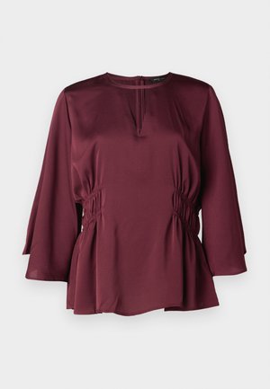 Blouse bordeaux avec un col rond, des manches longues en forme de cloche et des détails froncés sur les côtés. Fabriquée en tissu lisse avec une coupe décontractée.