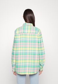 Chemise à carreaux dans des teintes de vert, jaune, rose et bleu. Design à boutons, manches longues, col ajusté et coupe décontractée. Tissu texturé.