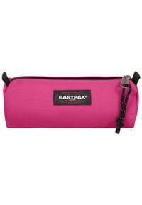 Růžový penál vyrobený z odolné tkaniny, s horním zipovým uzávěrem, černými kovovými doplňky a značkovou etiketou s embosovaným logem.