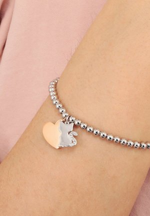 Silver beaded bracelet with heart and cat-shaped charm featuring rhinestone details worn on a wrist against pink fabric background.