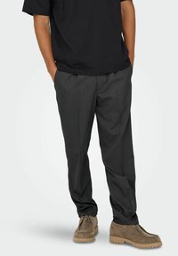 Grau zugeschnittene Hose aus leichten Stoff, mit geradem Bein Design und Frontfalten, kombiniert mit braunen Wildlederschuhen.