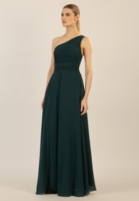 Ein schulterfreies Abendkleid in dunkelgrün mit plissiertem Oberteil und fließendem Rock. Hergestellt aus weichem, leichtem Stoff mit glatter Textur.