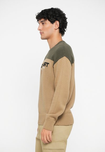 Jersey de punto con un cuerpo beige y hombros verde oliva, con puños y dobladillo acanalados, que muestra un logo en negro contrastante.