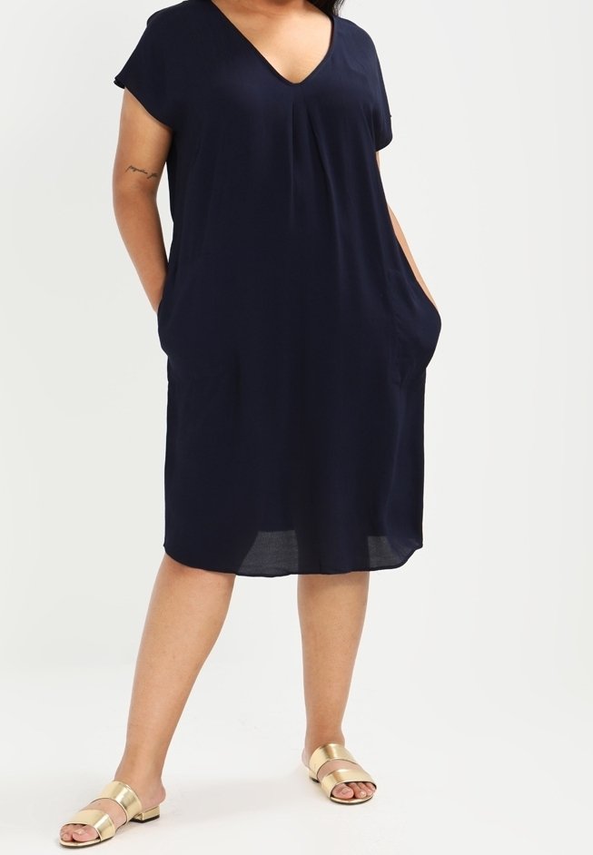 Navy blue short-sleeve dress with a V-neck, side pockets, and a loose fit. Soft fabric with a smooth texture and a knee-length hem.