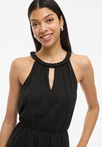 Fekete nyakpántos ruha fonott dekoltázzsal, kulcslyuk-áthallással és rugalmas derékpánttal. Simás textúra, légies sziluett, és nincs látható minta.