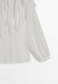Blusa bianca con scollatura arricciata, maniche lunghe a palloncino e orli elasticizzati, realizzata in un tessuto leggero e semitrasparente.