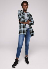 Camicia di flanella a quadri neri e azzurri chiari, indossata sopra una maglietta graphic grigia. Abbinata a jeans skinny blu e sneakers nere.