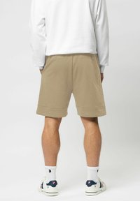 Beiga bomullsshorts med avslappnad passform, uppvikt fåll, sidofickor, kombinerat med vita strumpor och sneakers, sedd bakifrån.