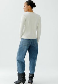 Lichtgrijze gebreide trui met golvende halslijn, gecombineerd met hooggerokte blauwe jeans en zwarte enkelboots met omgeslagen manchet.