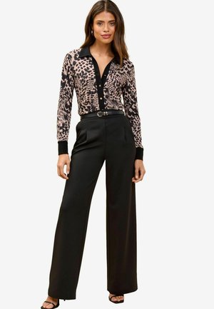 Camicia a maniche lunghe con bottoni in stampa animalier rosa e nera, abbinata a pantaloni larghi neri a vita alta e sandali neri.