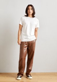 T-shirt en coton blanc, pantalon en cuir marron au toucher lisse, avec poches, associé à des baskets noires et blanches.
