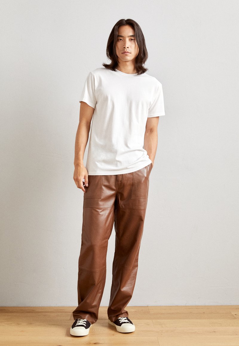T-shirt en coton blanc, pantalon en cuir marron au toucher lisse, avec poches, associé à des baskets noires et blanches.