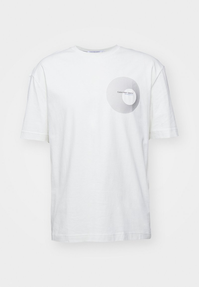 Valkoinen puuvillapaita, jossa on lyhyet hihat ja pyöreä pääntie. Paidassa on vasemmassa rintakehässä pyöreä harmaa kuvio ja teksti.