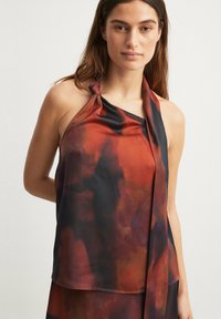 Halter neck top in lightweight fabric featuring abstract red, black, and purple watercolor patterns. Soft texture with a draped design.