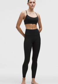 Czarny skrócony stanik sportowy i legginsy o wysokim stanie z subtelnym wzorem kropek; elastyczny materiał, dopasowany krój i minimalistyczne ramiączka.