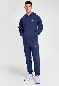 Mörkblå hoodie med känguruficka och dragsko, kombinerad med matchande joggingbyxor. Strukturerad tyg, med en logotyp på bröstet och låret.