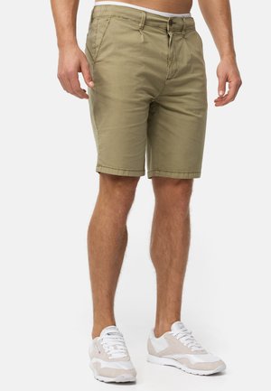 Khaki shorts med et glat stof, lynlåsåbning, sidelommer og lige snit, parret med hvide sneakers med beige detaljer.