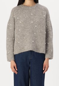 Pull en tricot gris à coupe décontractée, col rond et embellissements en perles. Tissu texturé avec des manches longues et des poignets côtelés.