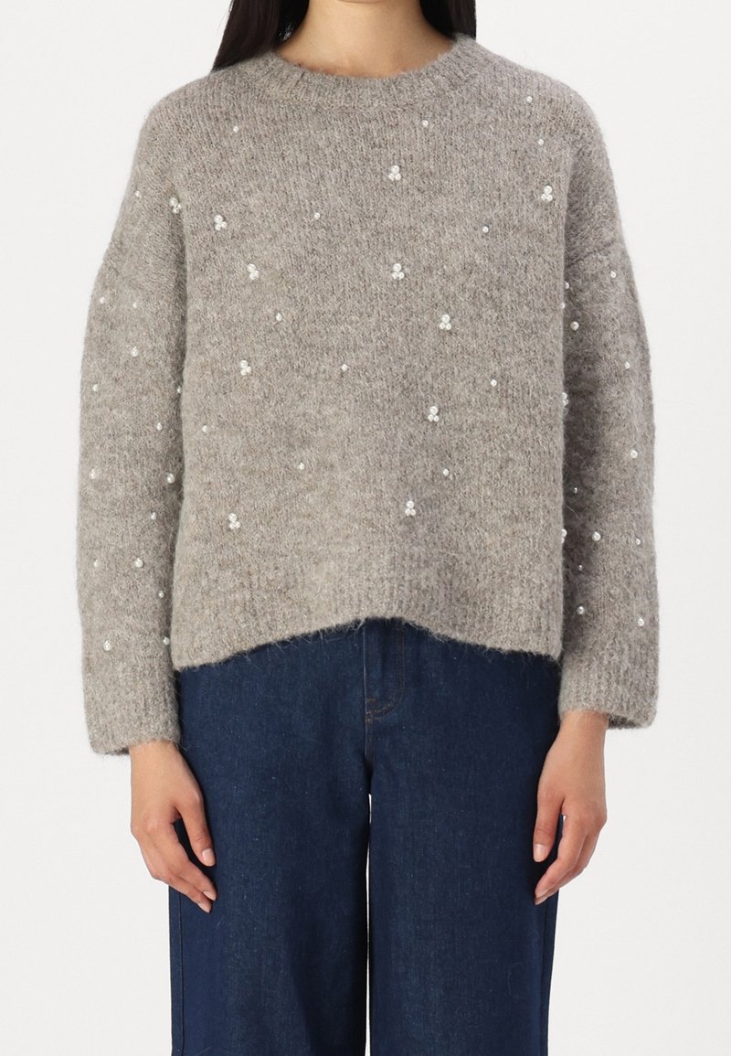 Pull en tricot gris à coupe décontractée, col rond et embellissements en perles. Tissu texturé avec des manches longues et des poignets côtelés.