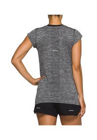 Kvinna iklädd grå kortärmad träningsskjorta och svarta shorts, sedd bakifrån med en hand på höften, mot vit bakgrund.