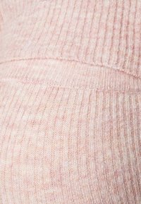 Mjukt rosa ribbat stickat tyg med synliga sömdetaljer, som visar textur och närbild på materialets väv.