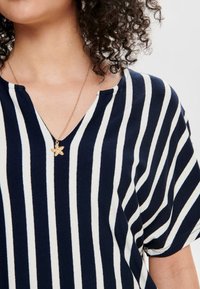 T-shirt de mangas curtas às riscas azul marinho e brancas com decote em V, feita de tecido suave e acompanhada de um colar com um pequeno pendente em forma de estrela dourada.