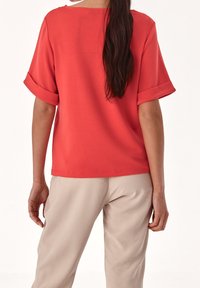Korallefarbenes Shirt mit kurzen Ärmeln und umgeschlagenen Bündchen, lockere Passform und glatte Textur. Kombiniert mit beigen Hosen, zeigt einen lässigen Stil.