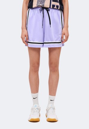 Personne portant un short de sport violet clair avec des rayures noires et blanches, des chaussettes Nike blanches et des baskets blanches avec des semelles en gomme.
