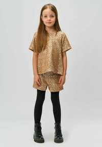 Top corto de manga corta dorado con lentejuelas y pantalones cortos, combinados con medias negras y botas con cordones. El conjunto presenta un acabado brillante y texturizado.
