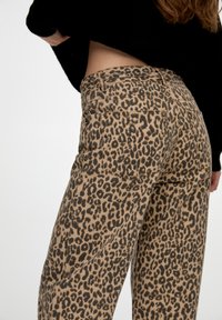Pantalon imprimé léopard en marron clair avec des taches marron foncé, doté d'une taille haute, cinq poches et une coupe droite.